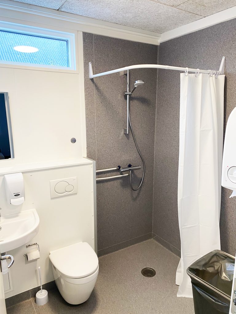 Badeværelse i modulbygning med toilet, håndvask og bruseniche med forhæng.